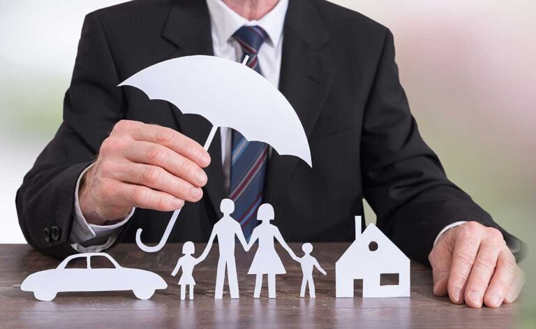 A person reviews auto insurance documents at a kitchen table, calculator and car keys nearby.